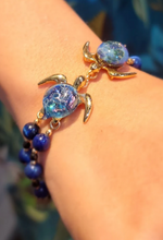 Akoni Gold double sea turtle bracelet with blue glass shells and two rows of dark-blue beads worn on a wrist.