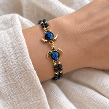 Hana Gold double turtle bracelet with almost-black blue glass shells and large aqua inclusions, worn with twin black bead strands.