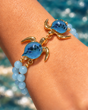 Mahalo double sea turtle bracelet with sky-blue glass shells and smooth pale-blue beads, shown in Gold on a wrist.
