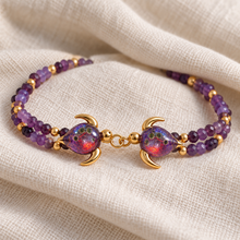 Malama Gold double turtle bracelet with plum-purple glass shells, green inclusions and red-orange highlights, on cream linen.